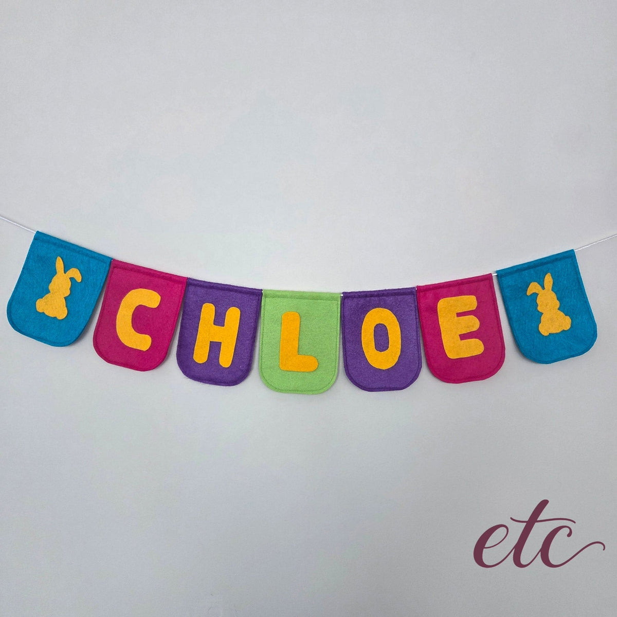 Personalised felt bunting / garland with 'CHLOE' letters and two bunnies on a plain background.