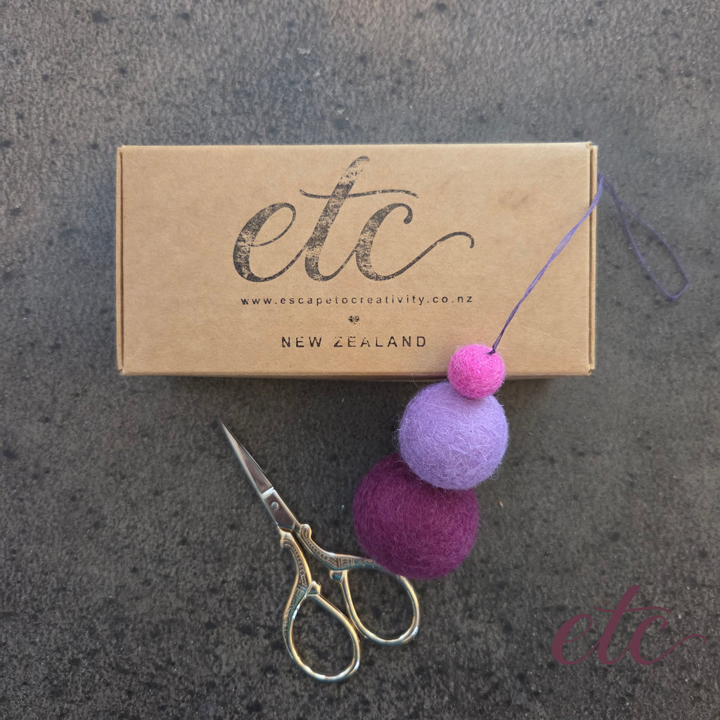 three purple shade felt balls with a cardboard package