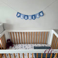 Personalised felt bunting / garland with 'Florian' letters on a plain background above a crib.
