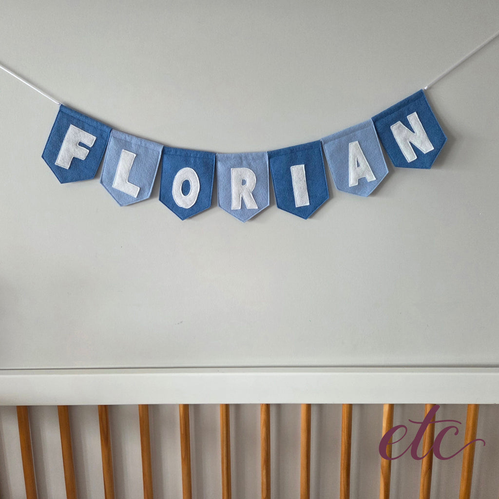 Personalised felt bunting / garland with 'Florian' letters on a plain background above a crib.