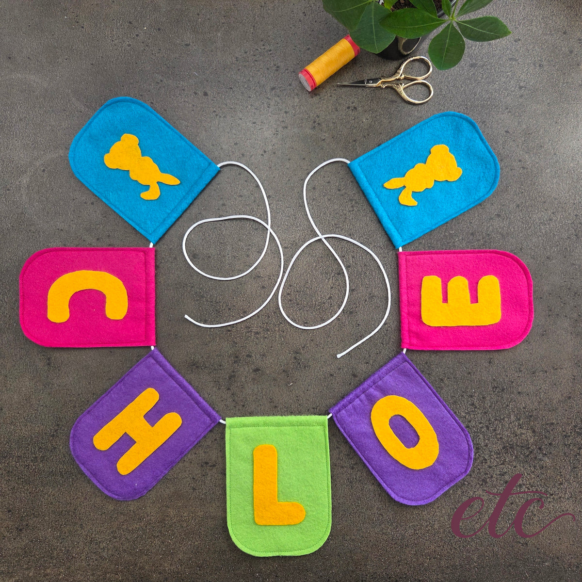 Colorful felt banner spelling 'CHLOE' with a bunny illustration on a gray surface.