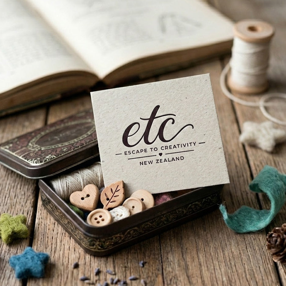 Small tin box with decorative items and a card on a wooden surface, featuring Gift card  Escape to Creativity New Zealand'.
